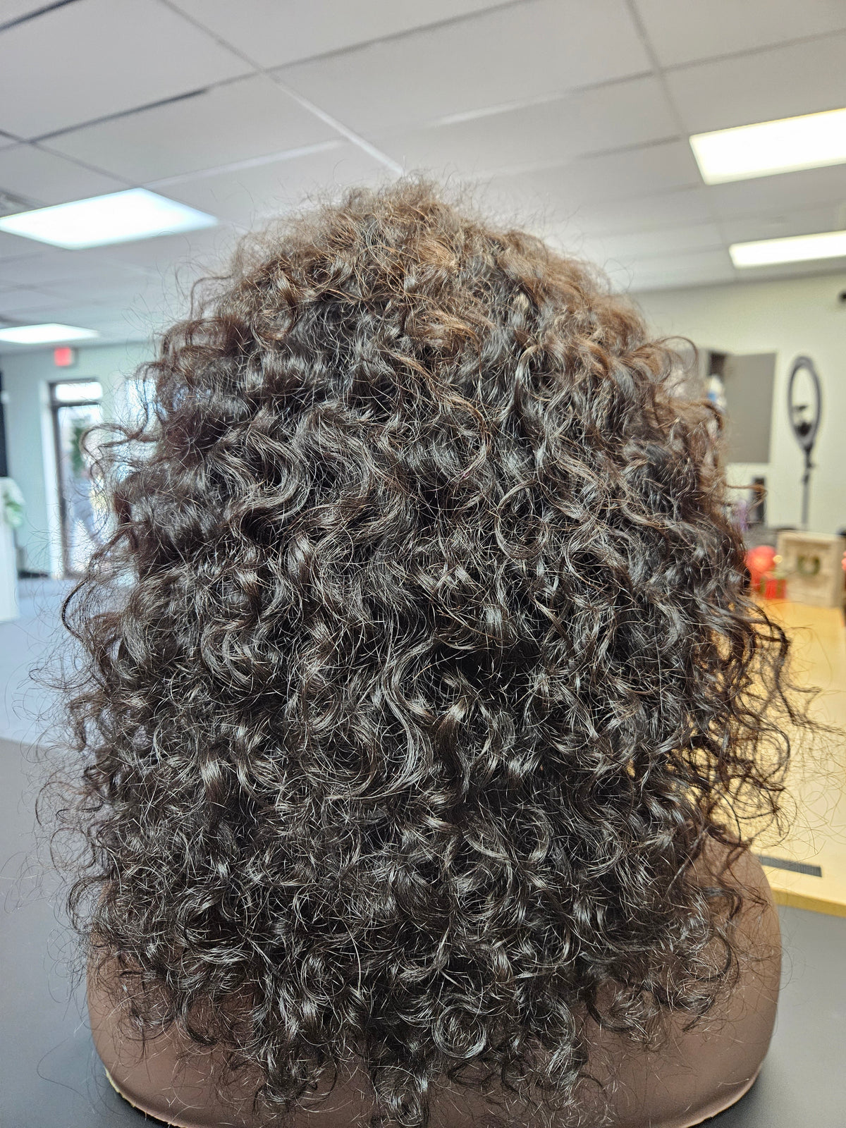A 12-inch natural black curly wig displayed on a mannequin head, featuring a realistic hairstyle with a flat surface.